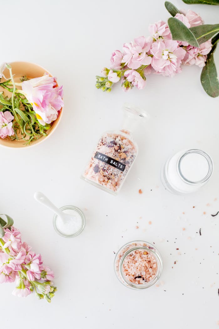 Top view of fresh delicate Brompton stock flowers with pink petals placed on white table with various jars of bath salts