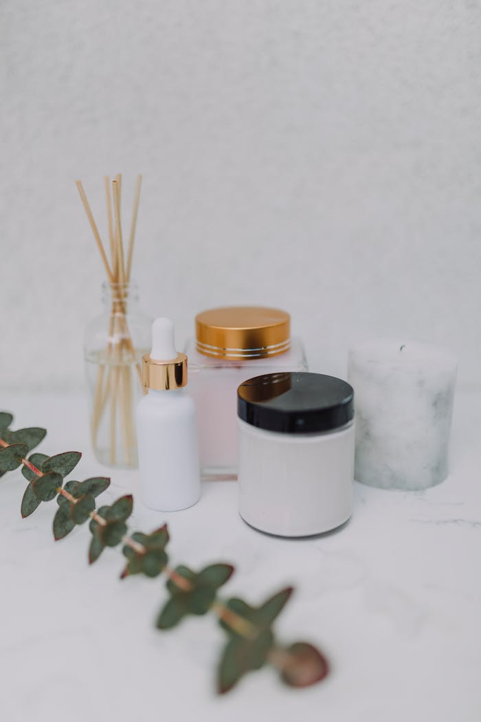 Minimalist display of skincare products, candle, and aromatherapy sticks on a marble surface.